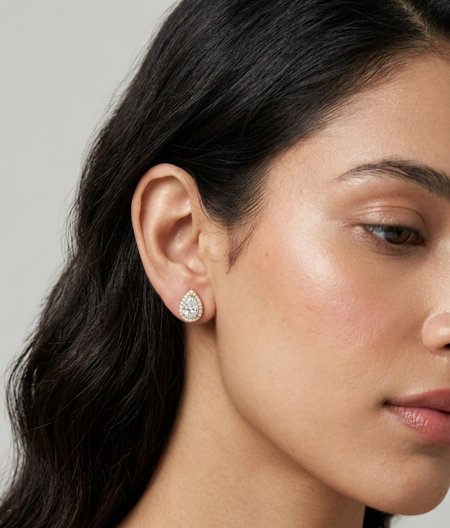 Pair of gold stud earrings featuring pear-cut clear stones encircled by a sparkling halo on a white studio background.