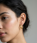 Pair of polished gold open hoop earrings with fluid sculptural curves shown on a pure white studio background.