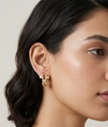 Pair of polished gold sculptural openwork earrings featuring bezel-set round clear stones on a white background.