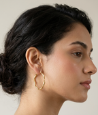 Pair of polished gold round hoop earrings featuring an organic wavy design displayed on a pure white studio background.