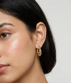 Pair of polished gold twisted croissant oval hoop earrings displayed against a plain white studio background.