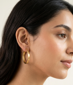 Pair of medium-sized oval hoop earrings featuring a brushed matte gold finish set against a pure white background.