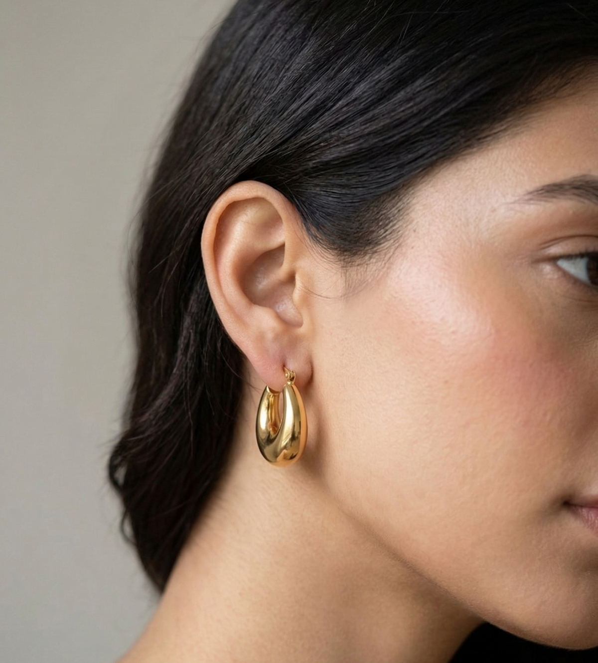 Model wearing Fluid curved gold-plated drop hoop earrings.