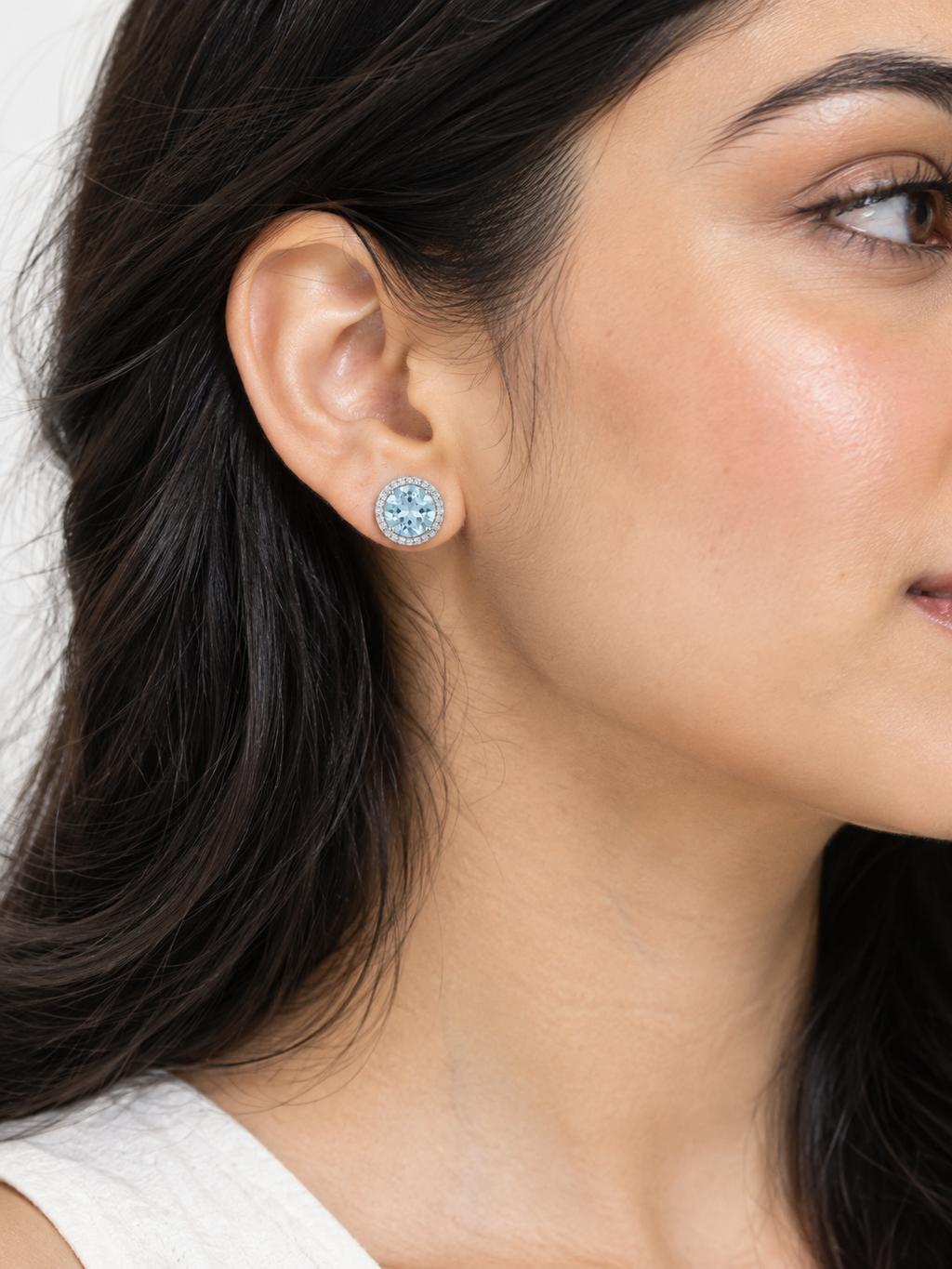 Pair of silver-tone stud earrings featuring round light blue aquamarine gemstones surrounded by clear pavé halos on a pure white studio background.