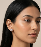 Pair of silver-tone stud earrings featuring round-cut clear gemstones enclosed in a cushion-shaped micropavé halo on a pure white studio background.